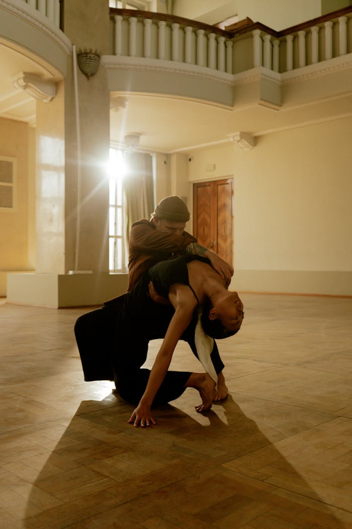 Elegant contemporary dance duo performing a dynamic pose in warm-lit interior space.